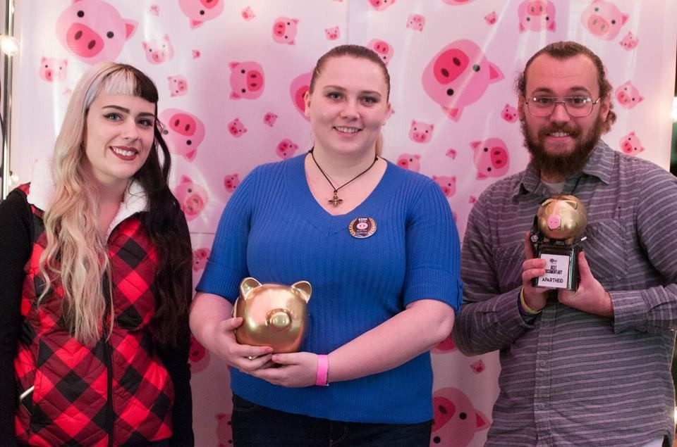 Image of a two female and one male OINK film festival participants holding trophies in front of a pig backdrop.