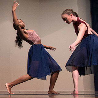 Two female students performing contemporary dance on stage.