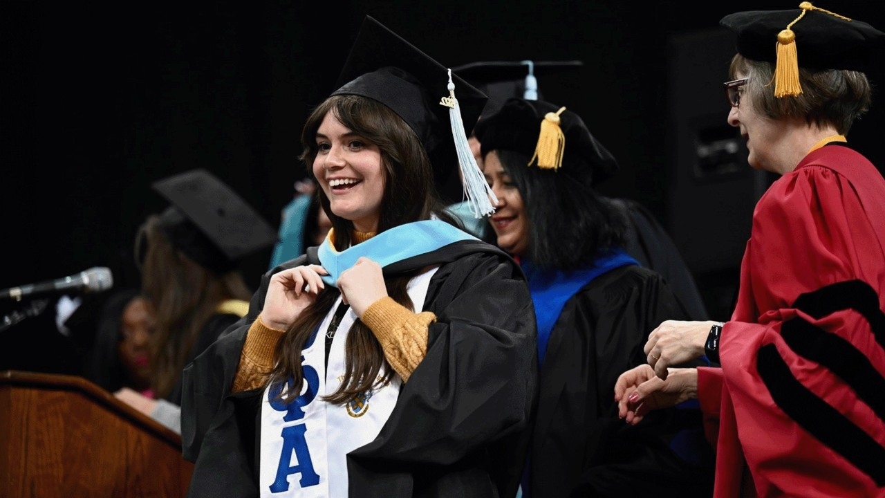 Student smiling as she recieves her diploma on stage.