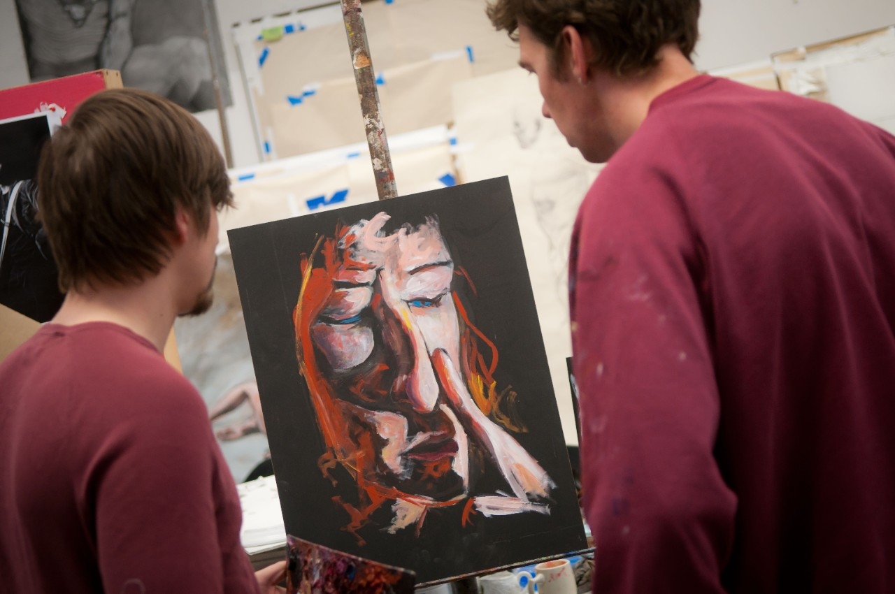 two students looking a painting of a man touching his nose 