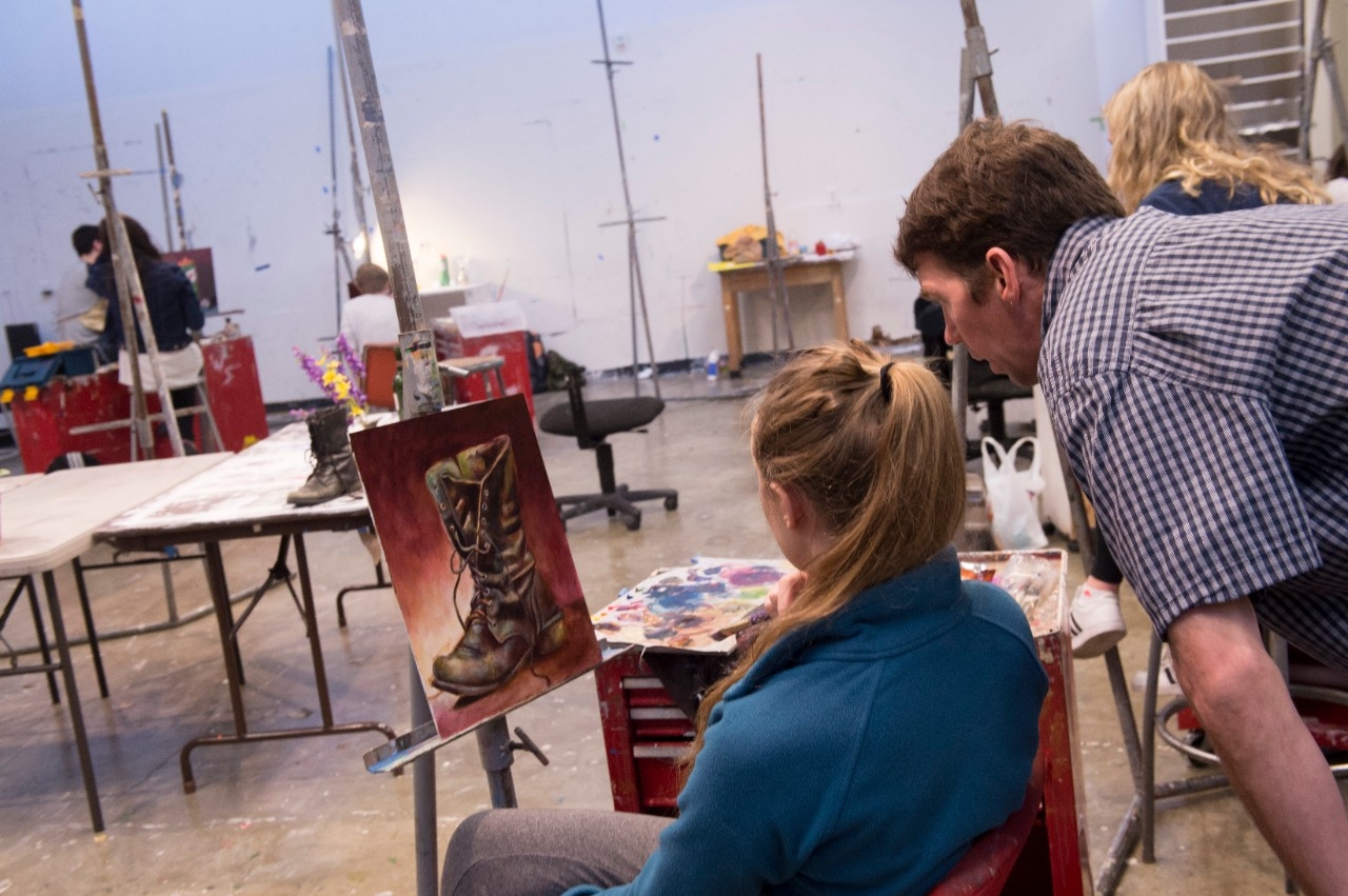 teacher and student looking at a detailed painting of a boot