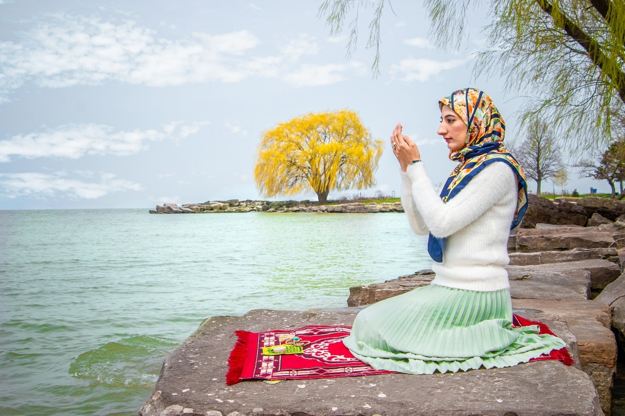 vibrant image of a woman praying sitting by a body of water