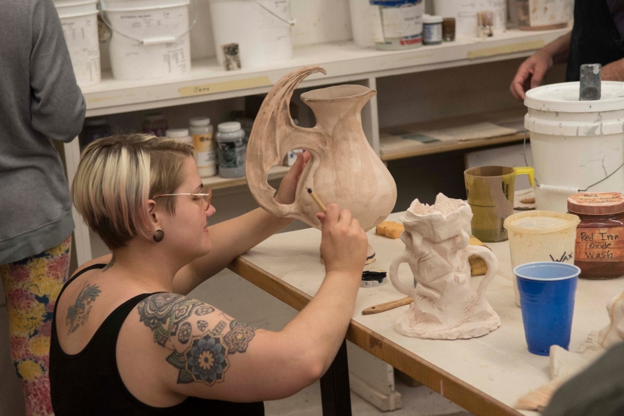 Student painting glaze on a ceramic pot