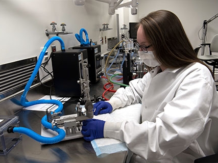 A student in protective lab gear using sophisticated laboratory equipment