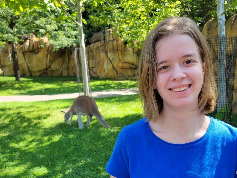 Adrienne Quiroz smiles outside with a kangaroo in the background.