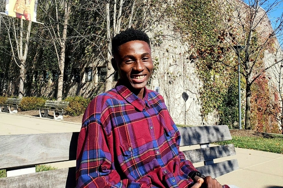 Joshua Osakwe smiles while sitting on a bench outside