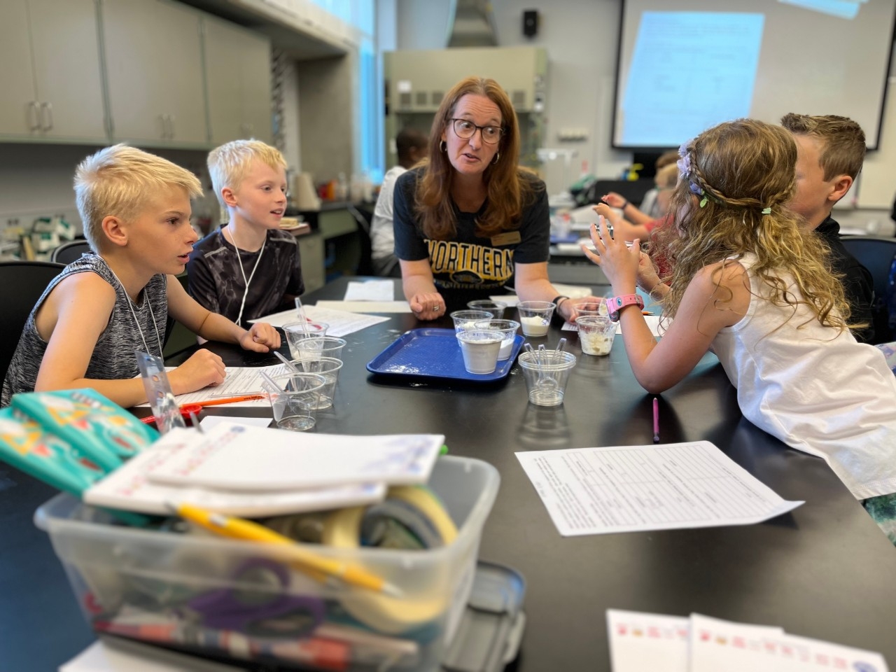 Young campers have an engaging discussion with a camp leader while doing an experiment