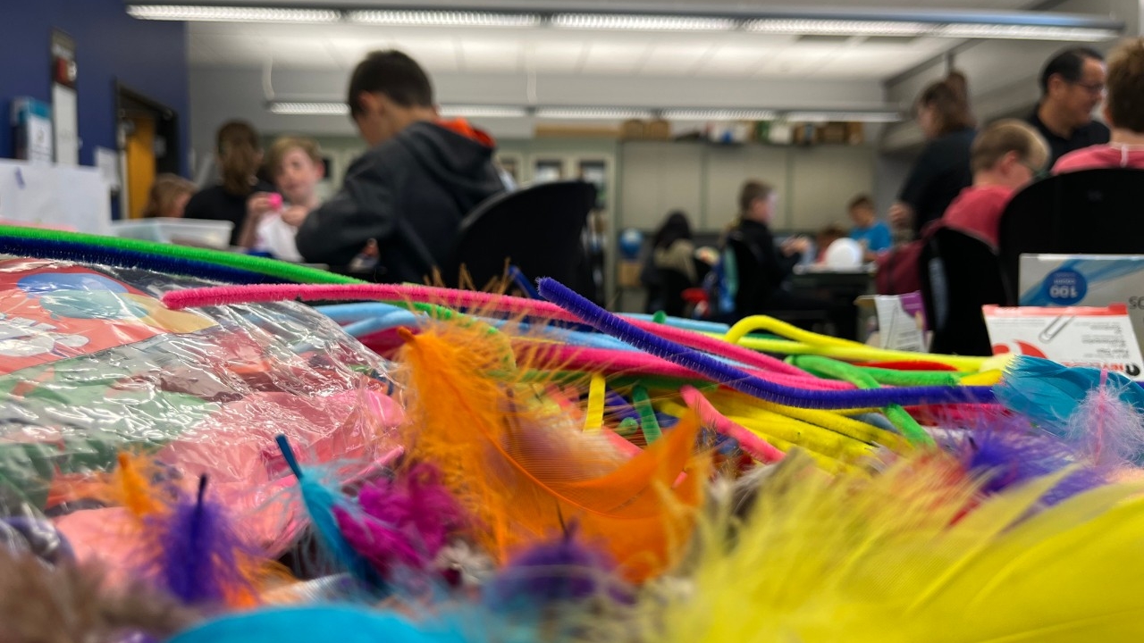 Up close image of colorful craft supplies with elementary school students in the background