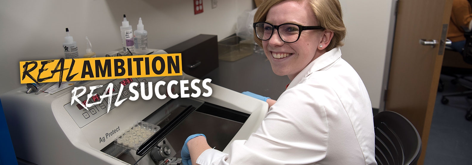 Female student in a lab coat smiling and she works with a Cryostat machine.