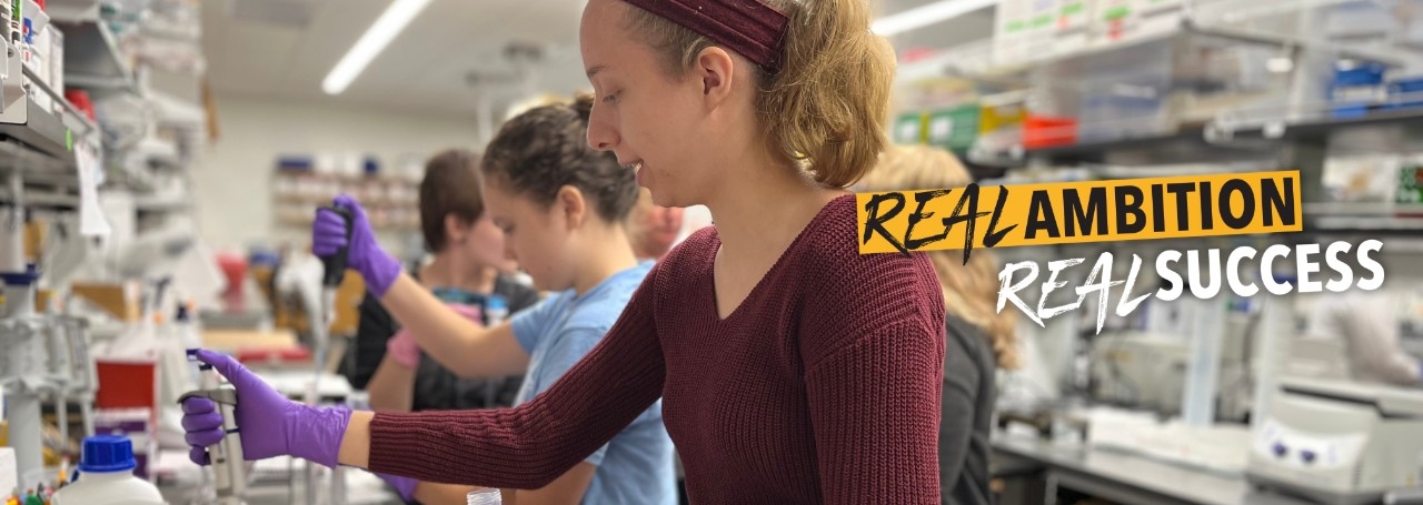 Up-close photo of plants in NKU's greenhouse with NKU's tagline, "Real Ambition, Real Success"