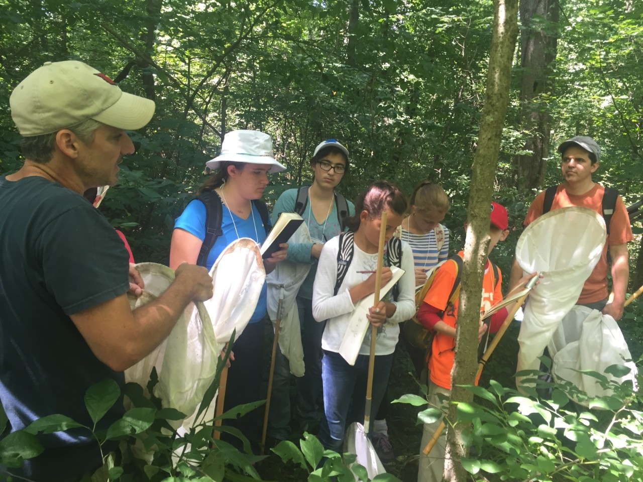 Visitors of NKU REFS hold butterly nets in the woods while listening to the guide's instructions.