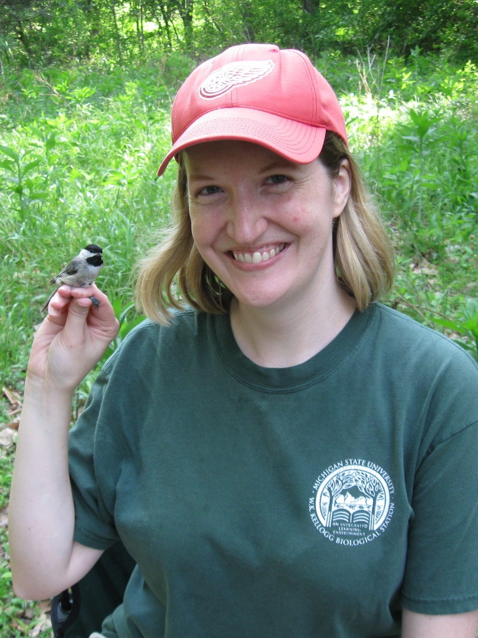 Photo of Dr. Walters, outside in a grassy area, with a small bird sitting on her fingers.