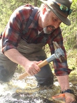 Photo of Dr. Durtsche hammering a rock in a creek.