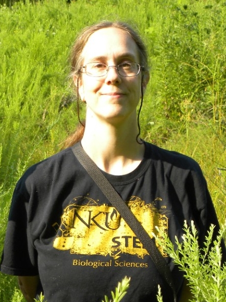 Photo of Dr. Whitson outside against a backdrop of vibrant green plant life.
