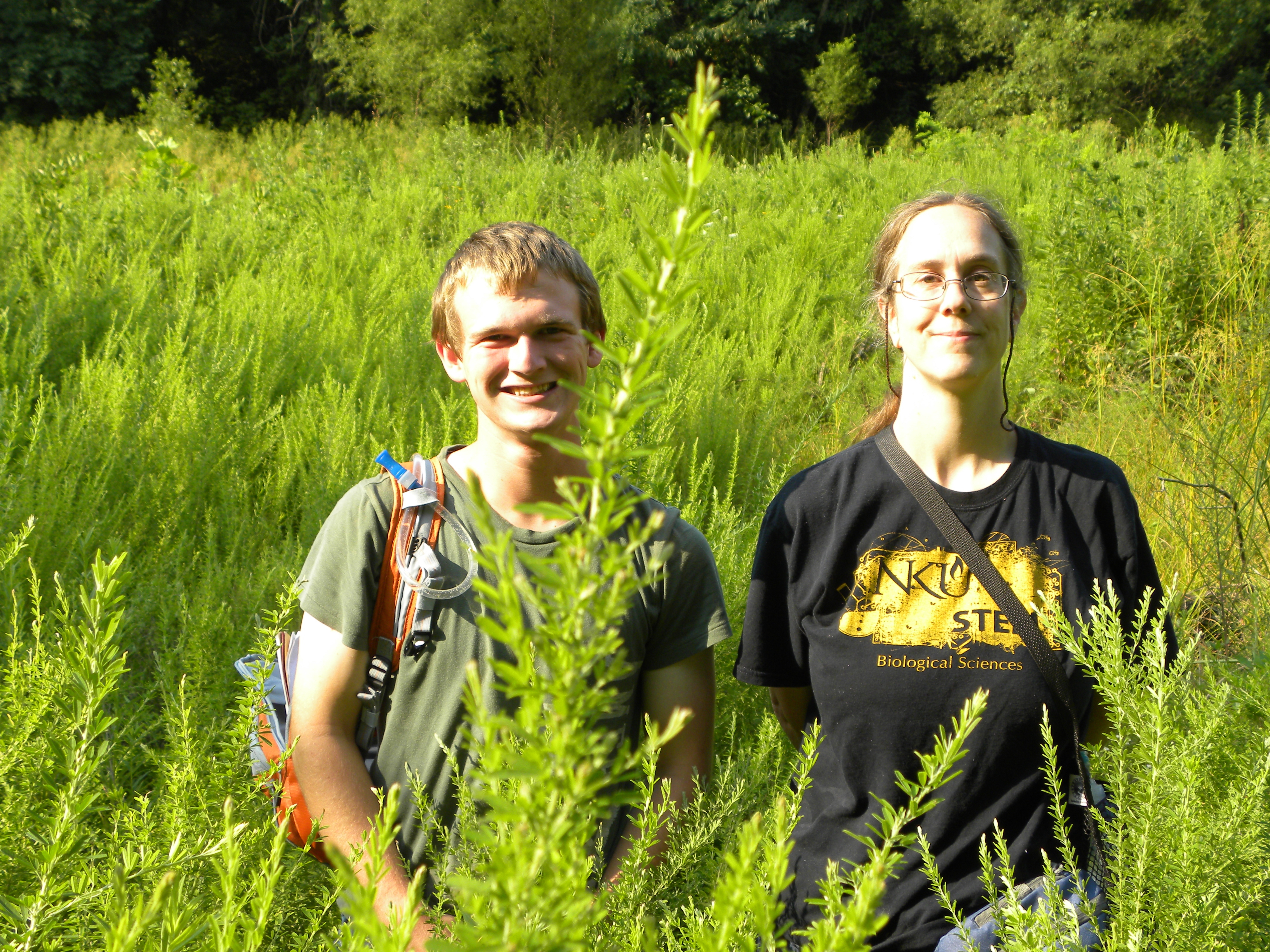 A photo of Dr. Whitson standing outside in tall grass with a student.