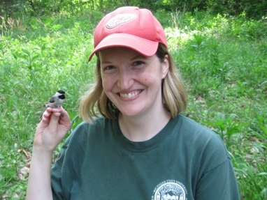 Photo of Dr. Walters, outside in a grassy area, with a small bird sitting on her fingers.