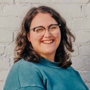 Sydney Gregory smiles in front of a brick wall.
