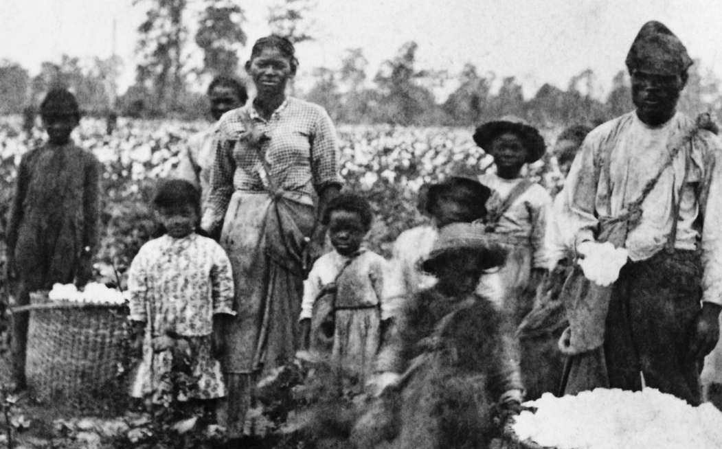 A group of slaves, two adults and several children, standing in a field.