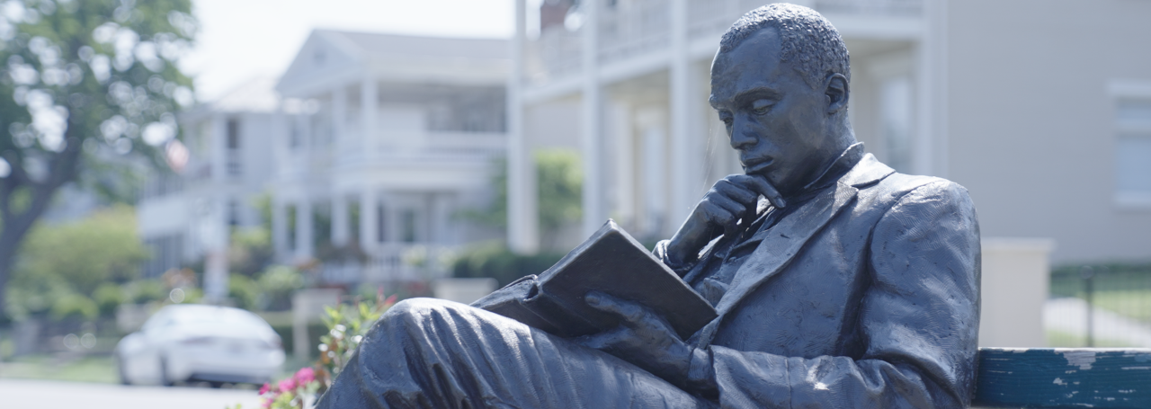 Statue of James Bradley, sitting on a bench reading a book.