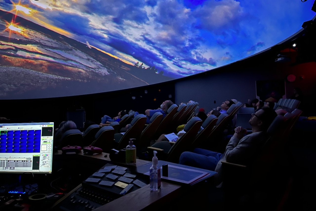 Planetarium visitors gaze at the dome-shaped screeen which featuring a vibrant sunset.