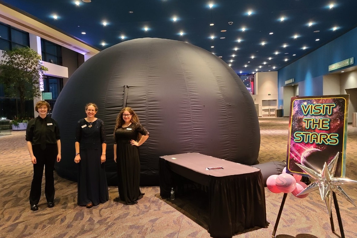Planetarium staff smile in front of the Roaming Dome at a private event in a convention center.