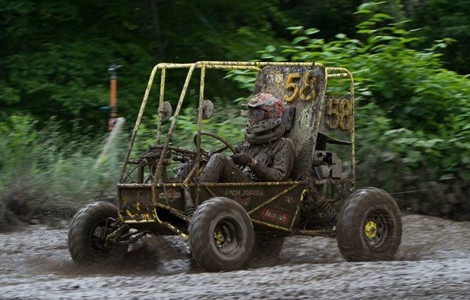 A muddy student driving the baja vehicle through the mud