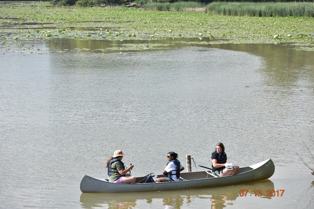 3 students collect water samples from a canoe
