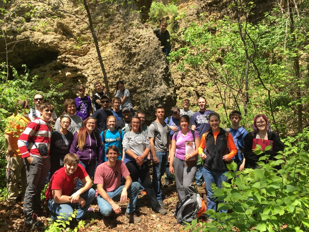 A class poses in front of a tree-covered outcrop of rocks