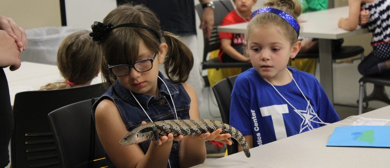 Image of two young children holding a lizard in a classroom