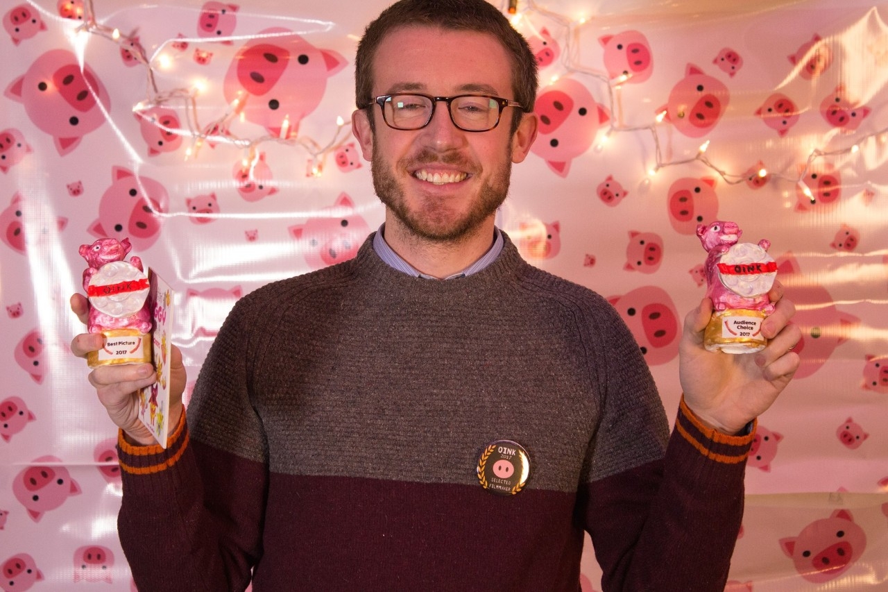 Image of a 2017 OINK film festival winning participant holding two trophies.