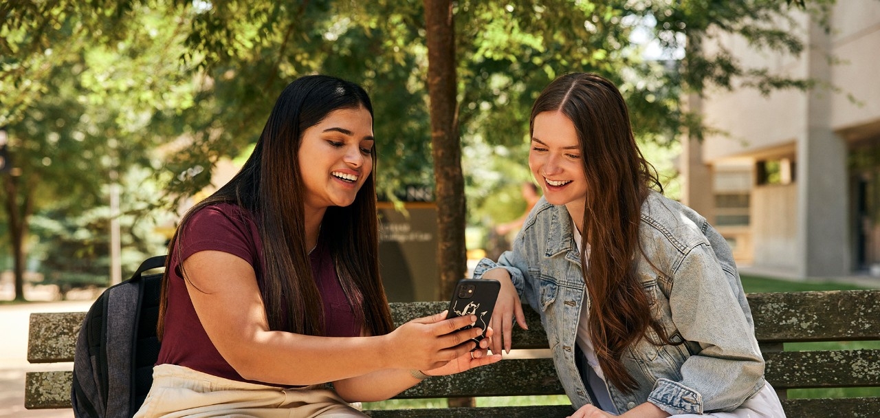 Two female students looking at a phone and smiling