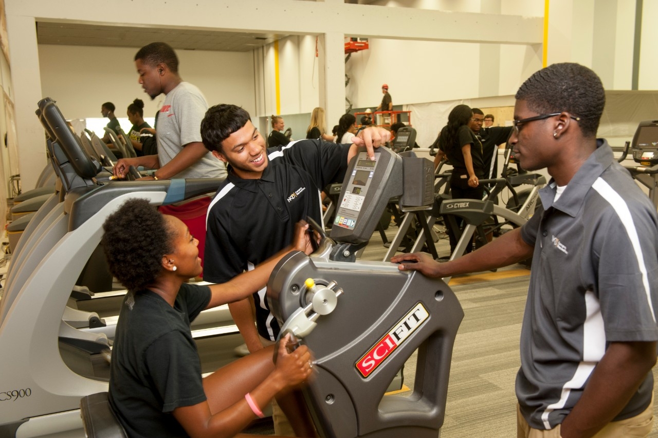 Campus rec assistants helping a student at an exercise machine.