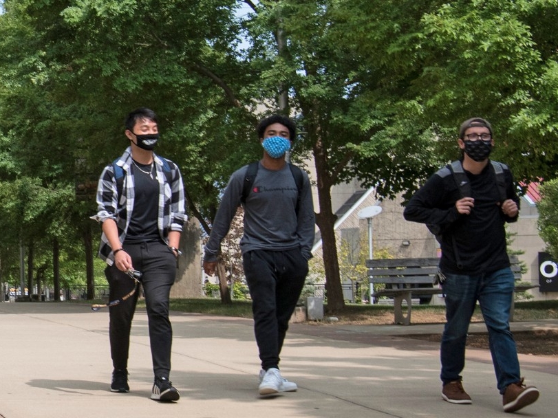 Three students wearing masks, walking down campus outside.