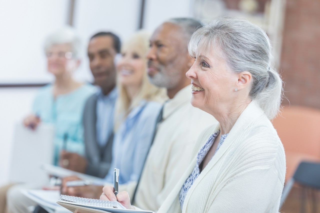 Smiling senior Caucasian woman attends a retirement planning seminar with her friends.