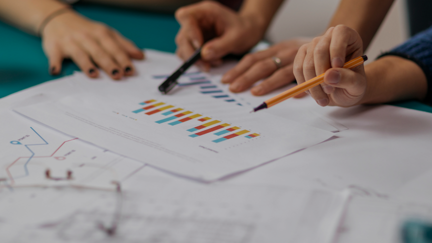 Two people holding pens point at a set of graphs