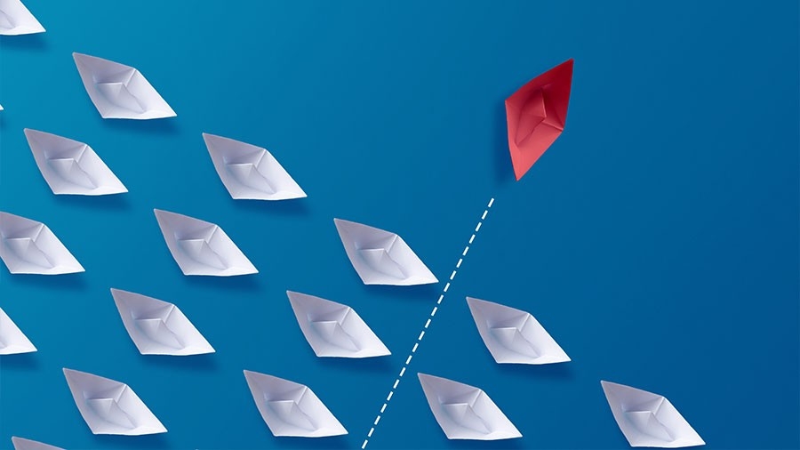 Red paper boat crossing in front of a group of white paper boats