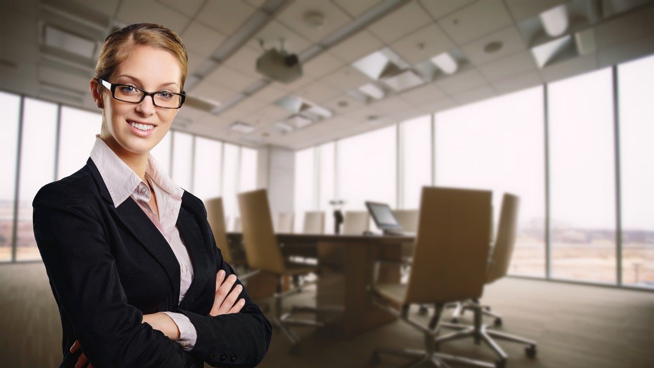 A woman in business attire standing in a conference room with floor to ceiling windows. 